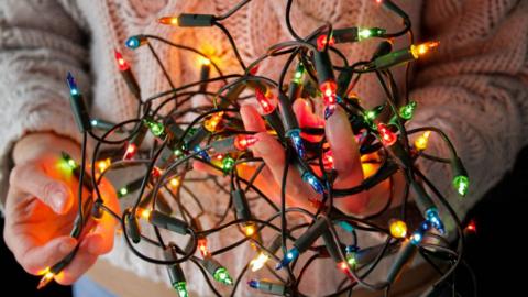 A close up of a person in a white jumper holding multi-coloured fairy lights