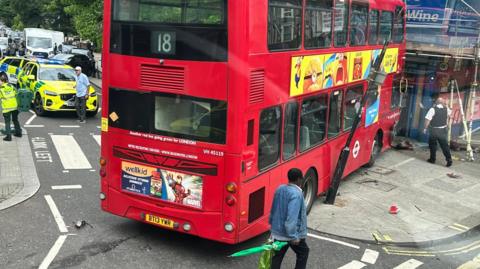 A red double-decker bus has mounted a pavement on the corner of a street and its front-end has hit scaffolding outside a shop