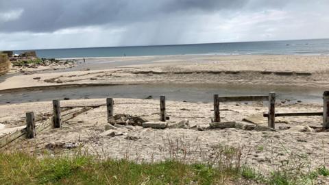 A beach with a series of wooden posts and an inlet of water