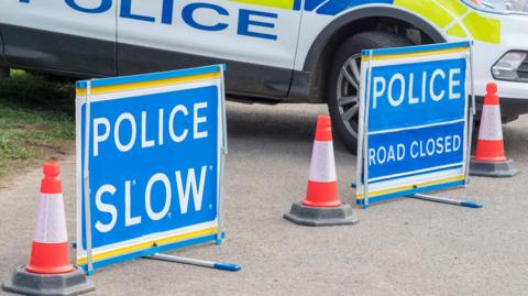 A stock image of a police car, with traffic signs stating 'police slow' and 'road closed'.