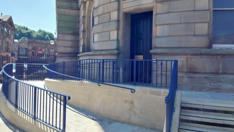 The rear entrance to Todmorden Town Hall, which now features a wheelchair ramp. Rails on the ramp and staircase are painted royal blue.