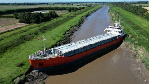 Orange cargo ship wedged diagonally across river.