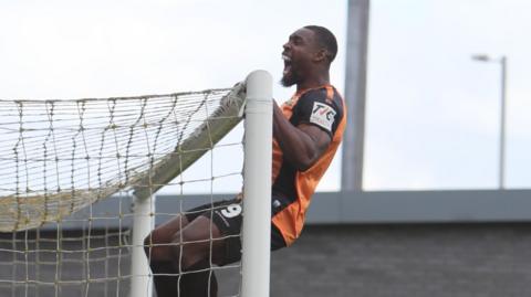 Barnet's Lee Ndlovu hangs on the crossbar as he celebrates scoring at Fylde
