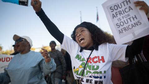 A woman punches the air, while holding a placard reading "South Africa is for South Africans" during an anti-migrant march.