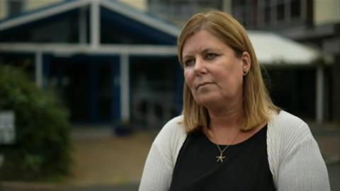 Julia Neal from Age UK has dark blonde hair to her shoulders and wears a light grey blouse over a black top with a gold necklace