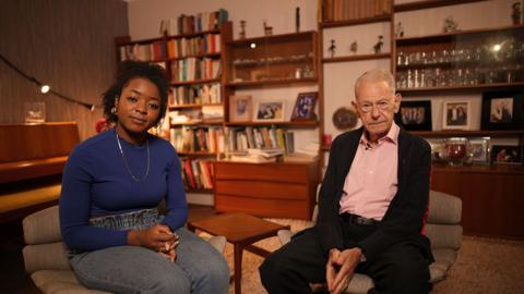 Emma-Louise Amanshia and John Hajdu sitting in a living room of a house.