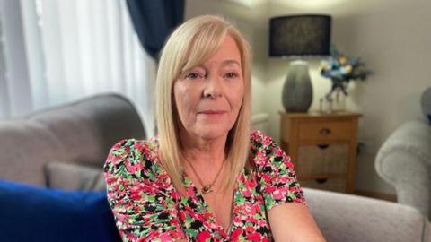 Sylvia Vickery, a woman with blonde hair looking directly to camera wearing a pink and green floral dress