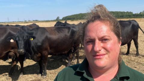 A woman wearing a green polo top standing in front of a herd of cows.