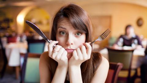 A young woman sitting in a restaurant, holding a knife and a fork