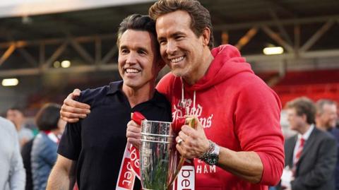 Rob McElhenney and Ryan Reynolds pose with the trophy following Wrexham's promotion to the Championship