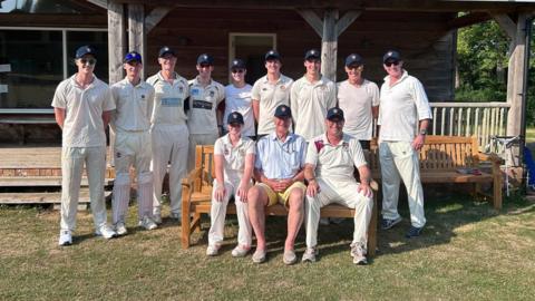 An older man surrounded by people in cricket gear.