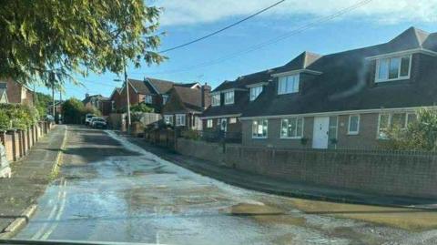 Water flowing down Edward Street - a residential street with detached houses one each side. 