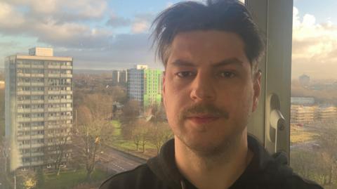 Photograph of Lukasz Ciszek in his 12th floor apartment in Manchester