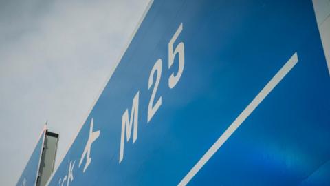 A portion of a blue M25 sign with grey sky seen behind it.