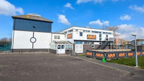 A picture of the Adur Outdoor Activities Centre which is currently closed. A number of signs with the centre name emblazoned in orange can be seen dotted around the centre.