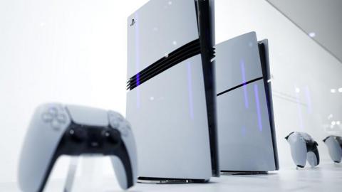 PlayStation 5 consoles next to controllers. They are white with black decals, set against a white background.