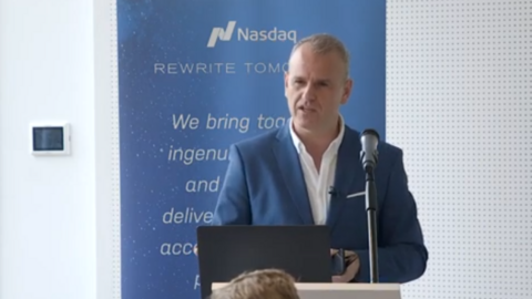 Simon Davies wearing a blue jacket over a white shirt, speaking from a podium