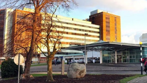 Altnagelvin Hospital is a large white and brown building with a large glass front entrance. 