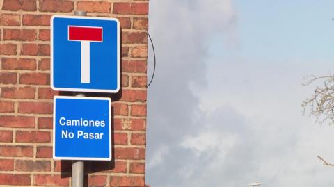A close-up of a blue and white road sign with 'Camiones No Pasar' on a separate square sign underneath a typical dead-end sign.
