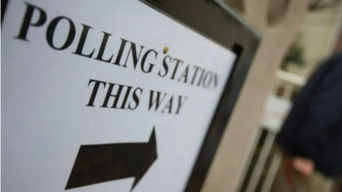 A sign with the words 'Polling station this way'. There is an arrow below it. 