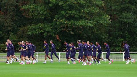 A group of players running across a football pitch during training