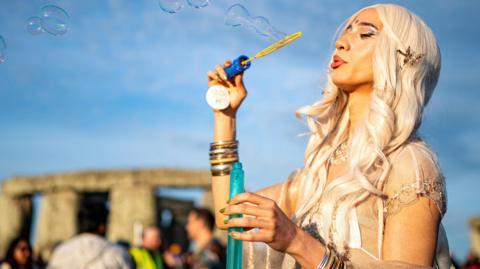 A woman blows bubbles stood in front of Stonehenge