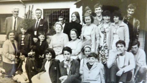 A black and white photo of a group of different age - with the children sitting on the ground