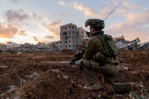 An image showing a crouching Israeli soldier looking at damaged buildings in Gaza