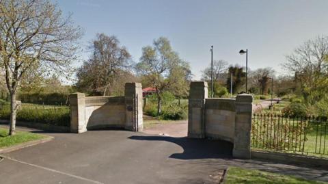 One of the entrances to Walker Park. Grassed areas and trees can be seen behind a stone-built gateway.
