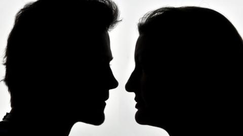 A side-profile silhouette of a man and a woman facing one another.