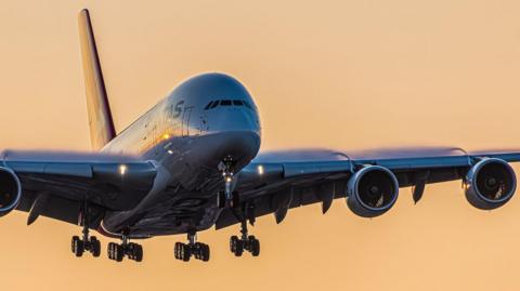 Close up shot of Qantas aircraft in the air overhead, silhouetted against an orange sky
