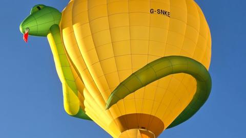 A yellow hot air balloon, with a green 3D snake wrapped around it