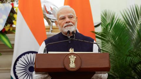 Indian PM Modi standing in front of two Indian flags