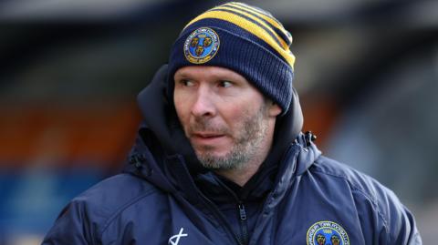 Shrewsbury Town head coach Michael Appleton watches on in his club coat and beanie