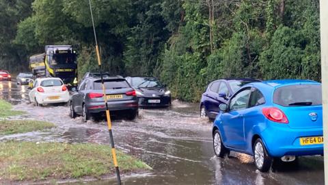 Cars drive through flood water on a busy road. 