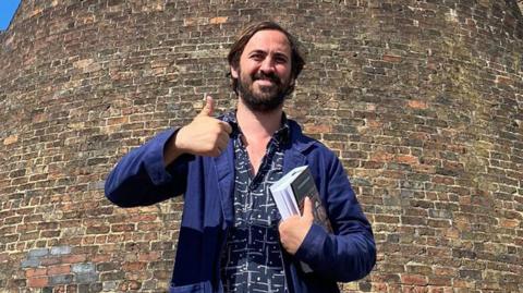 A man giving a thumbs up holding a book