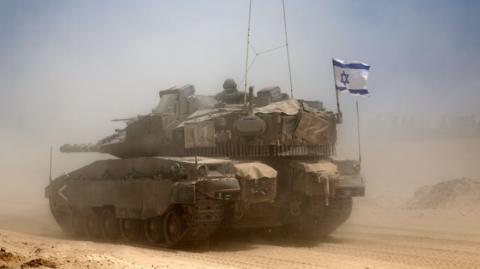 A tank raises dust on sandy ground.