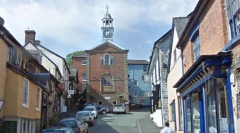 A narrow street rising up a hill with rows of buildings down both sides and a tall building at the top