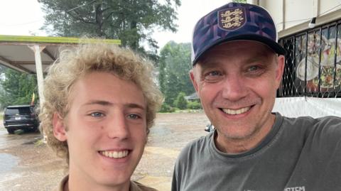 Iain Bagwell, right, is a man in his 50s. He takes a selfie with his teenage son, pictured left. Both smile for the camera.