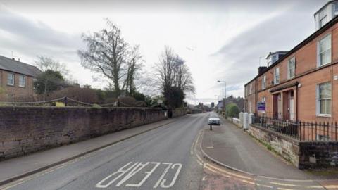 A landscape image of Laurieknowe road in Dumfries. There are houses both left and right of the road. The sky is cloudy.