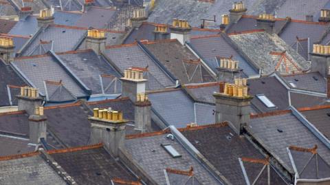 A large number of grey slated roofs with tall chimneys.