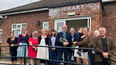 Group of people standing in front of the brick building of the library looking at the camera.