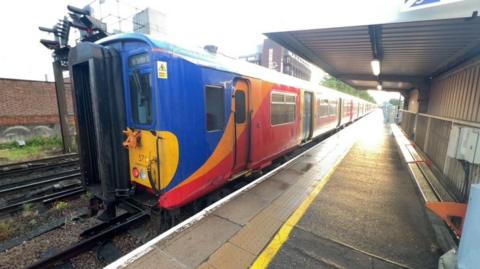 A train on a station platform with blue orange and yellow colours.
