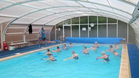 People do aerobics in the pool whilst being instructed by swim coach