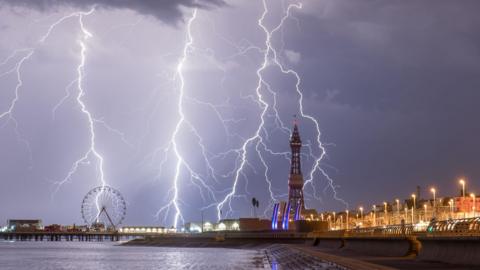 Three bolts of lightning strike on a grey sky over Blackpool skyline.