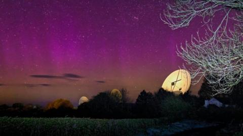 A photo of illuminated satellites in Madley Satellite Station under a purple and pink night sky