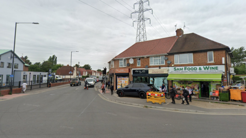 The road junction of Stoke Road and Elliman Avenue in Slough. It is a four-way junction with traffic lights. Along the road are a number of terraced houses.