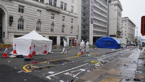 CSI police officers dealing with an incident near the Royal Liver Building in Liverpool during the Premier League winners' parade. There is much detritus lying on the road.