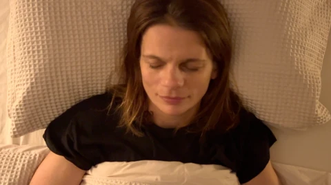 A woman with light brown hair and in black clothing sleeps