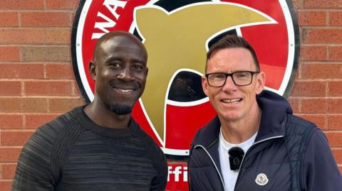 Albert Adomah and BBC WM's Darren Wrack standing in front of the Walsall FC sign at their Essington training ground